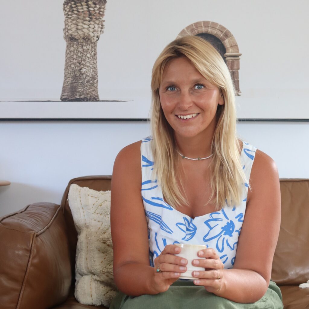 Katy Guildford - a business strategy & performance expert in New Zealand sat on a couch holding a coffee